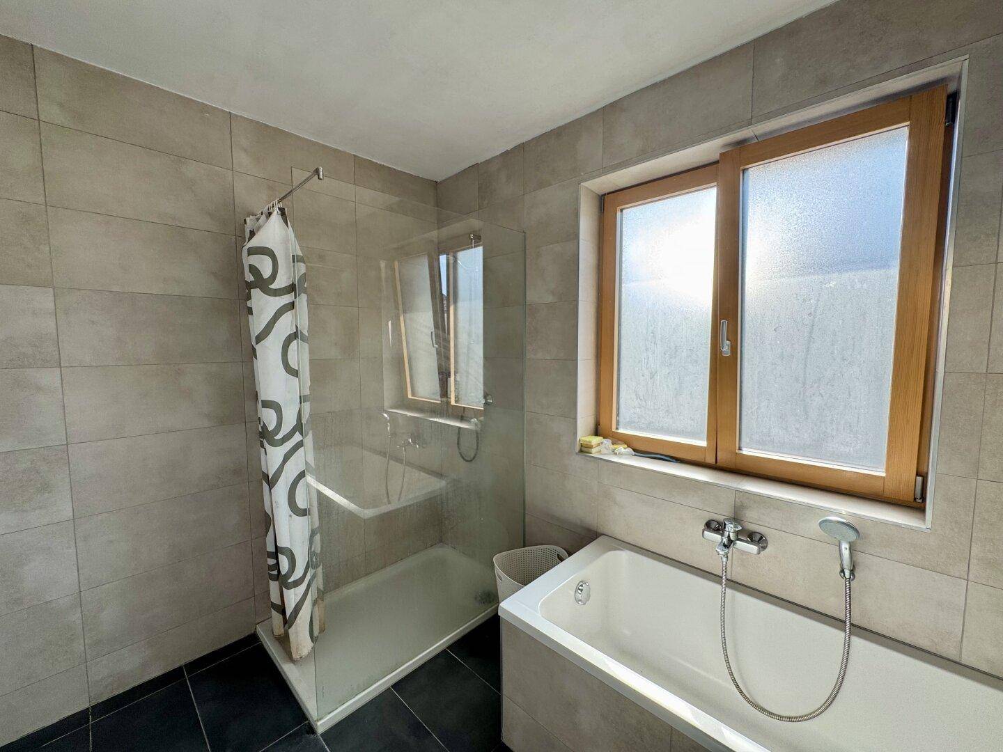 Helles Badezimmer mit Badewanne, separater Dusche und Fenster für Tageslicht.