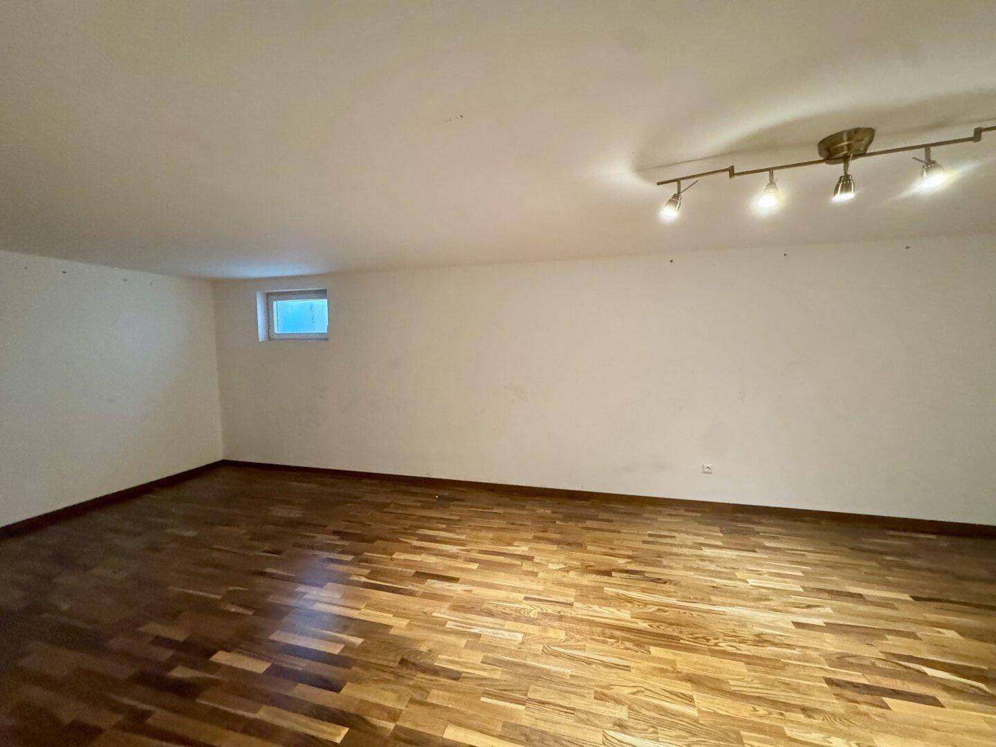 Ausgebauter Kellerraum mit Holzboden und einem kleinen Fenster für Belüftung.