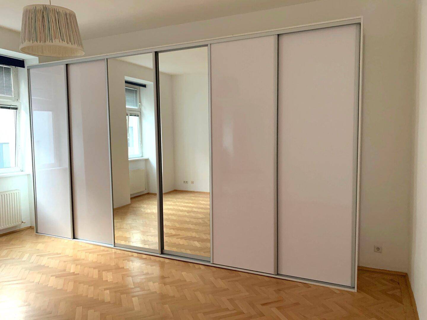 Großer, moderner Kleiderschrank mit Spiegeltüren und weißen Fronten im Schlafzimmer.