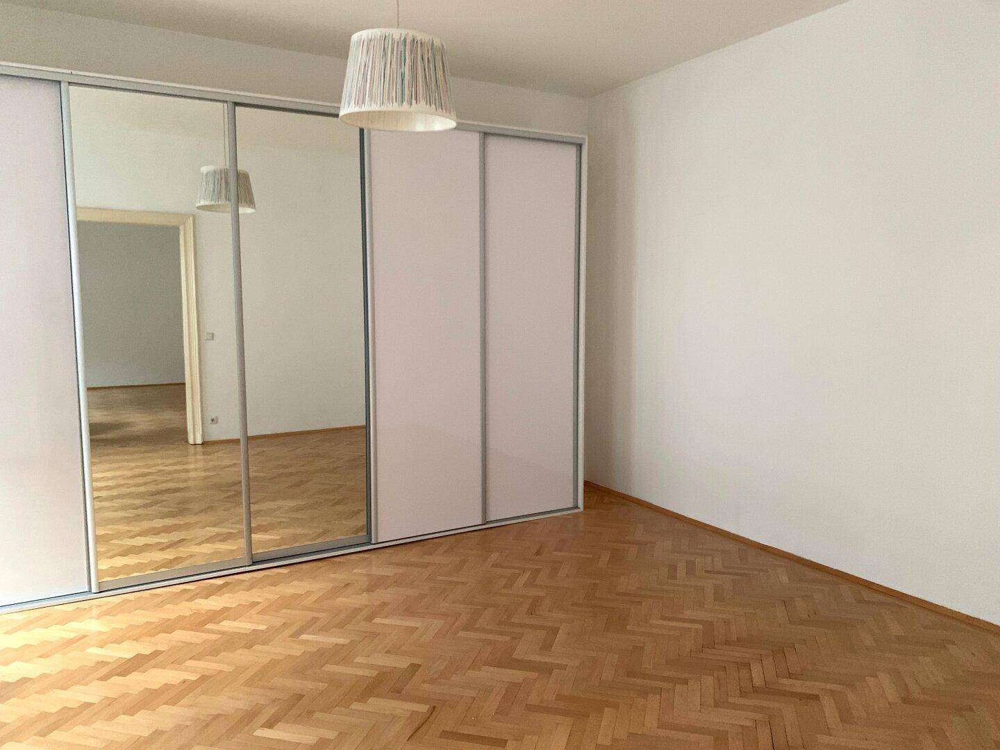 Schlafzimmer mit Fischgrätparkett und großem Spiegelschrank, Blick in den Flur.