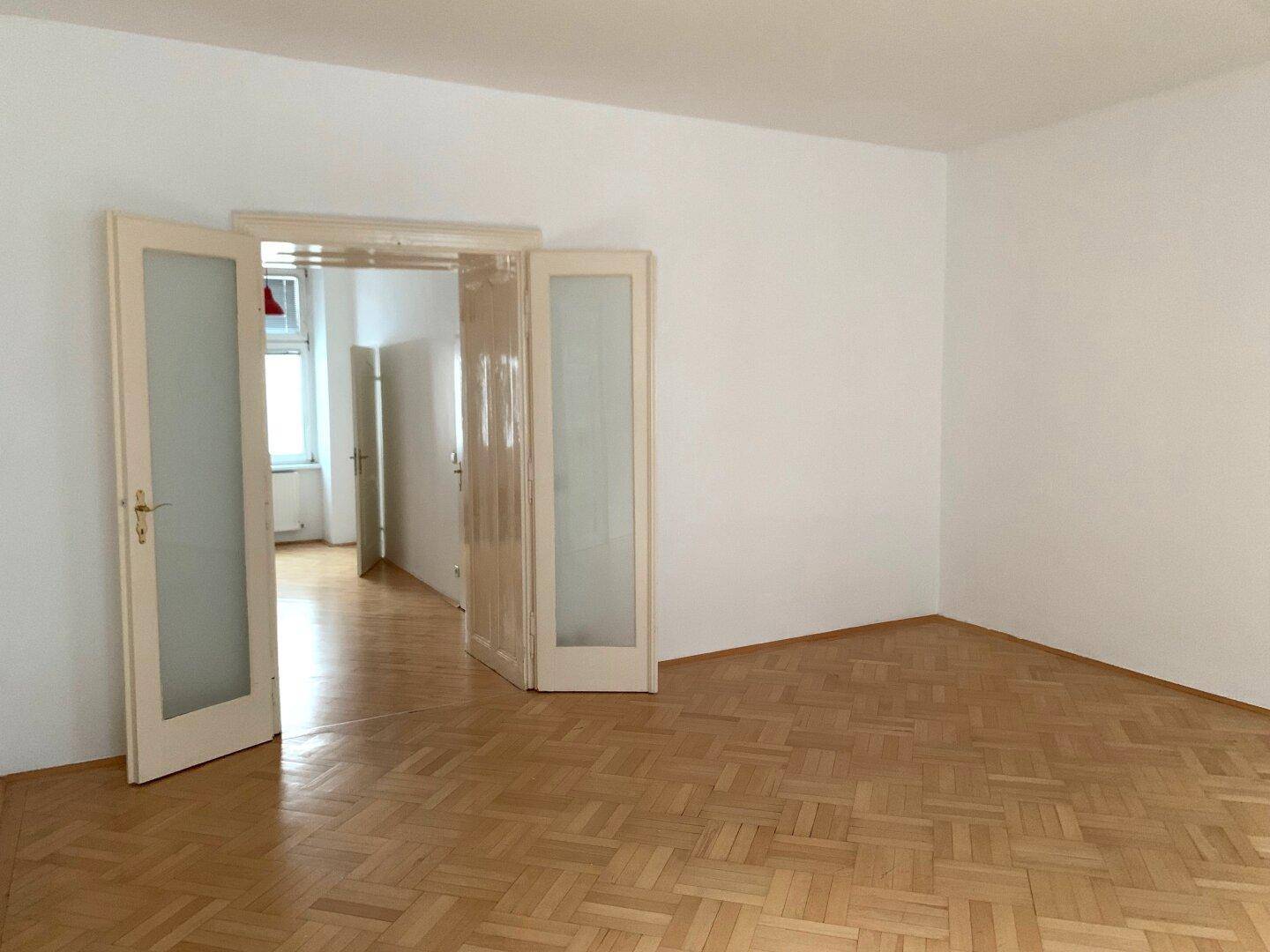 Helles Zimmer mit Fischgrätparkett und eleganten Doppeltüren zu einem angrenzenden Raum.