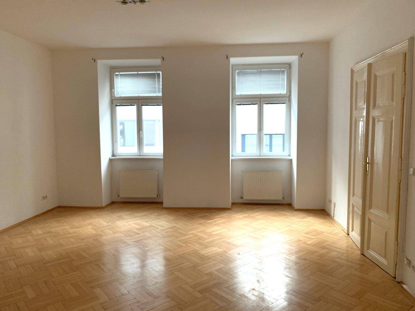 Großes, helles Zimmer mit Fischgrätparkettboden und zwei Fenstern, bereit zur Einrichtung.