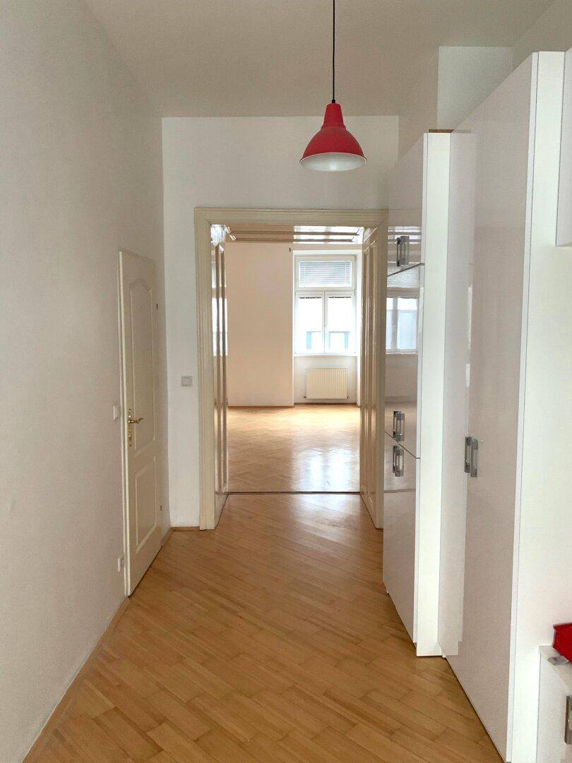 Heller Flur mit Fischgrätparkett, modernen weißen Einbauschränken und roter Pendelleuchte.