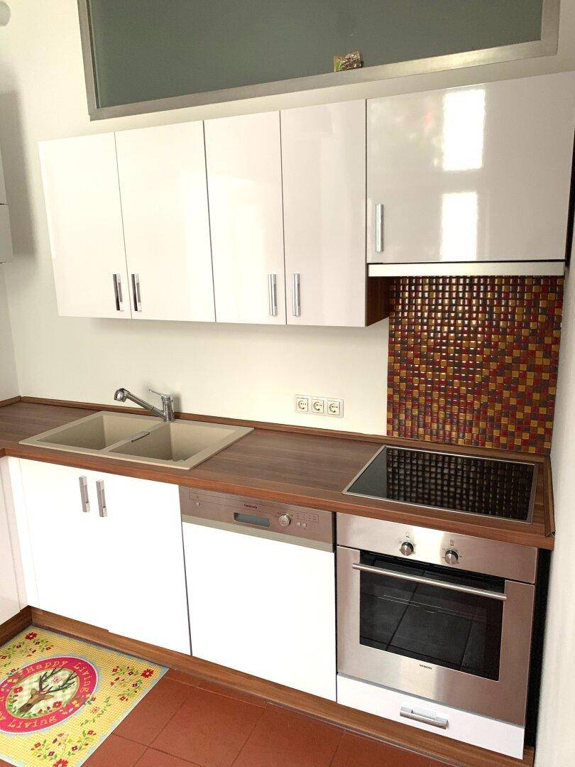 Moderne Küche mit weißen Schränken, Holzarbeitsplatte, Induktionskochfeld und Backofen.