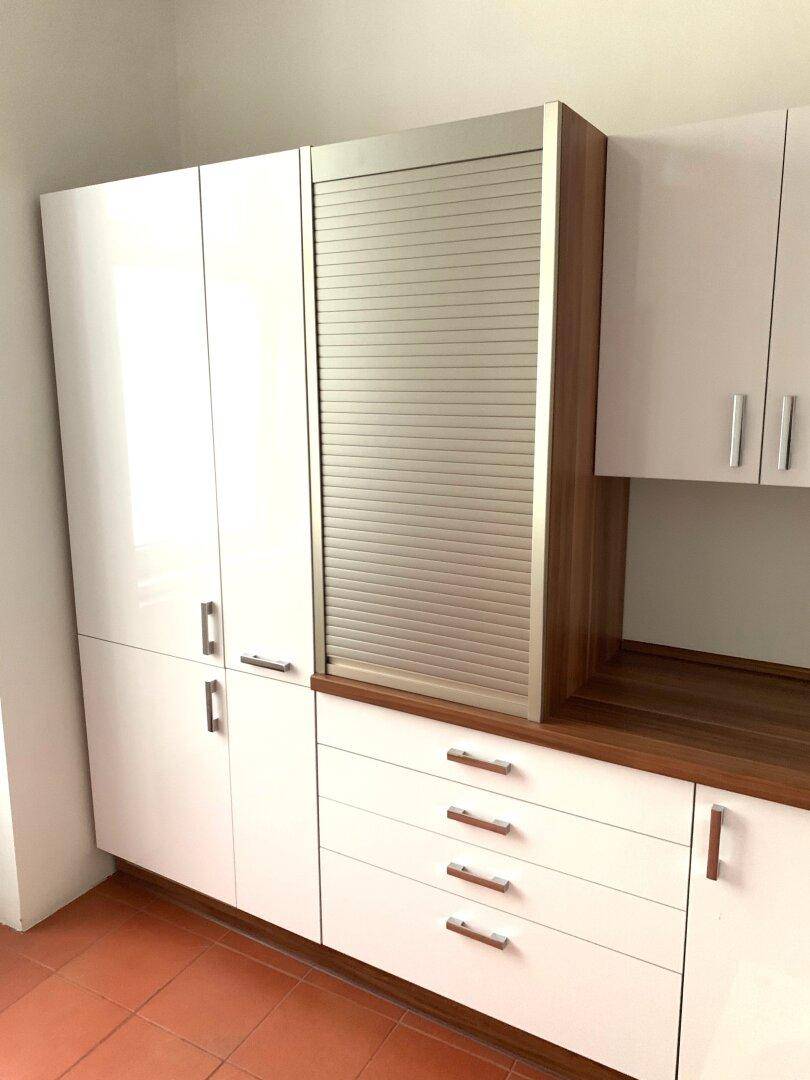 Weiße Küchenschränke mit Holzdetails und praktischem Rollladenschrank für zusätzlichen Stauraum.