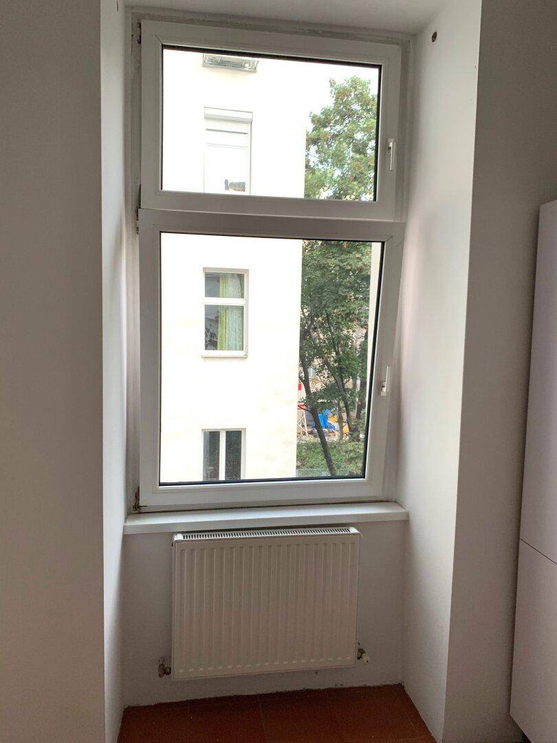 Fenster mit Blick auf einen Innenhof und grüne Bäume, sorgt für natürliches Licht.