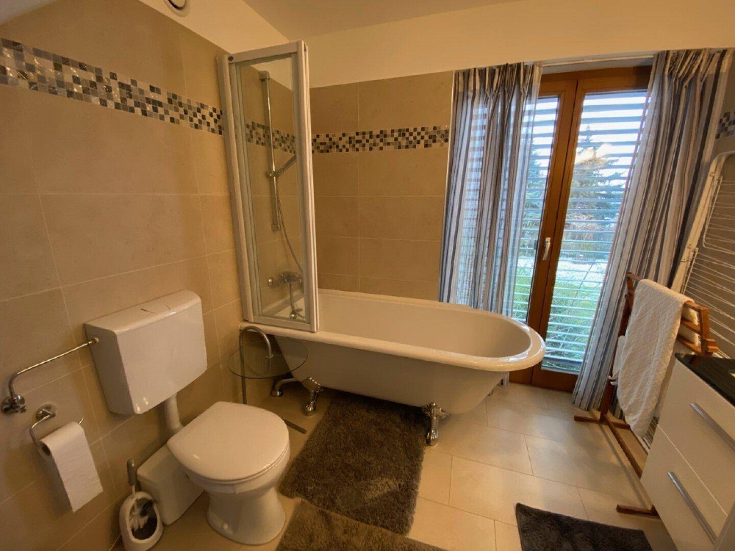 Helles Badezimmer mit freistehender Badewanne, WC und Fenster.