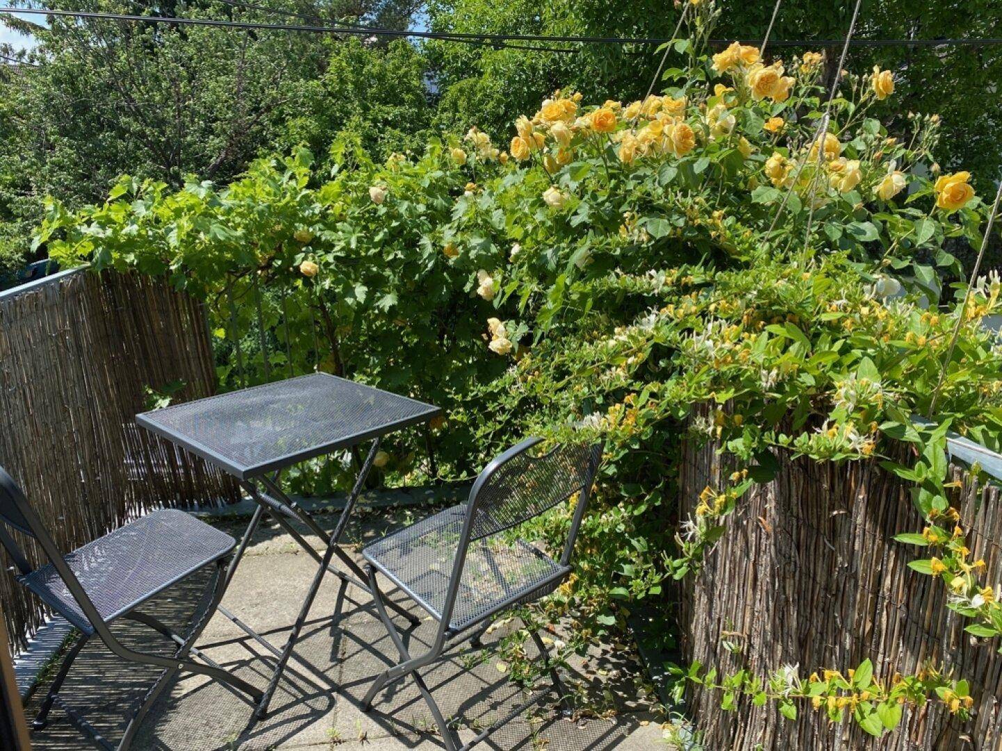 Kleiner Balkon mit üppiger Bepflanzung, Rosen und einem Bistrotisch.