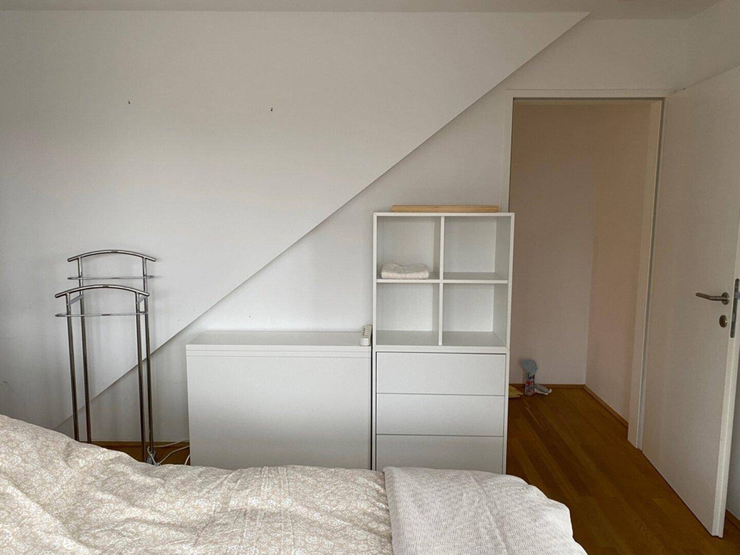 Schlafzimmer mit Dachschräge, weißer Einrichtung und Holzboden.