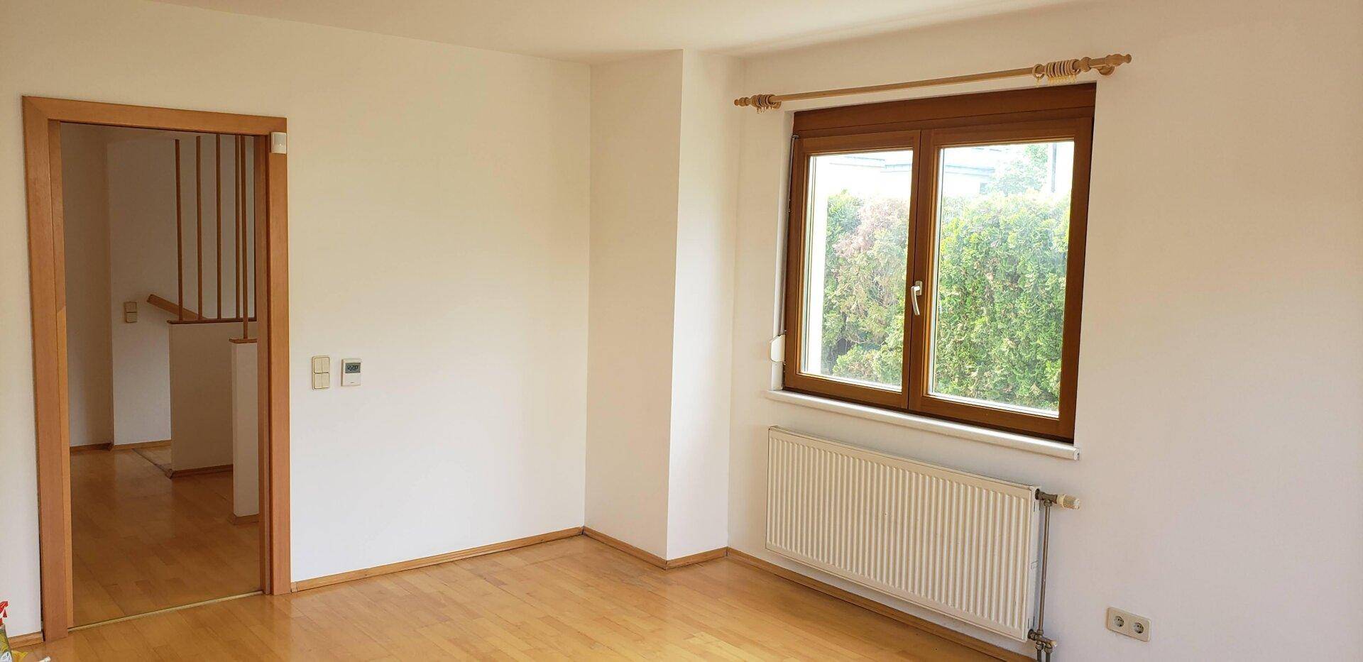 Heller Raum mit Holzfußboden, weiß gestrichenen Wänden und Blick ins Grüne.