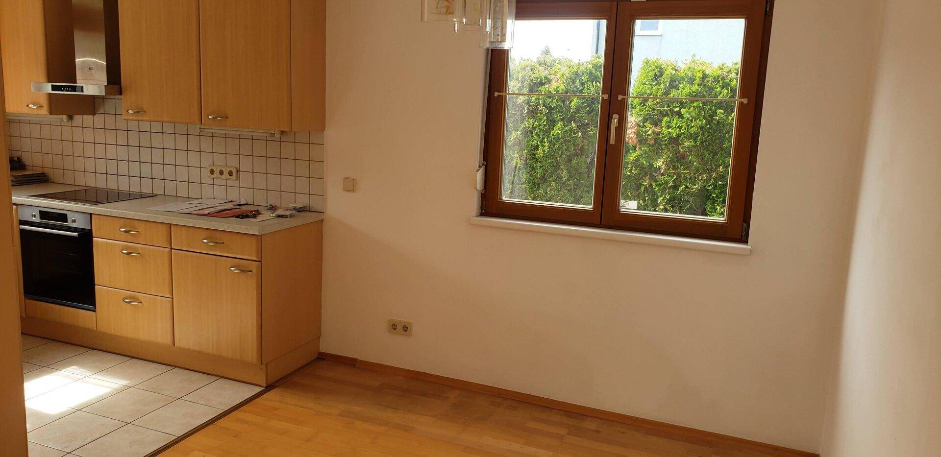 Funktionale Küche mit Holzschränken, Fliesenboden und Fenster mit Blick ins Grüne.