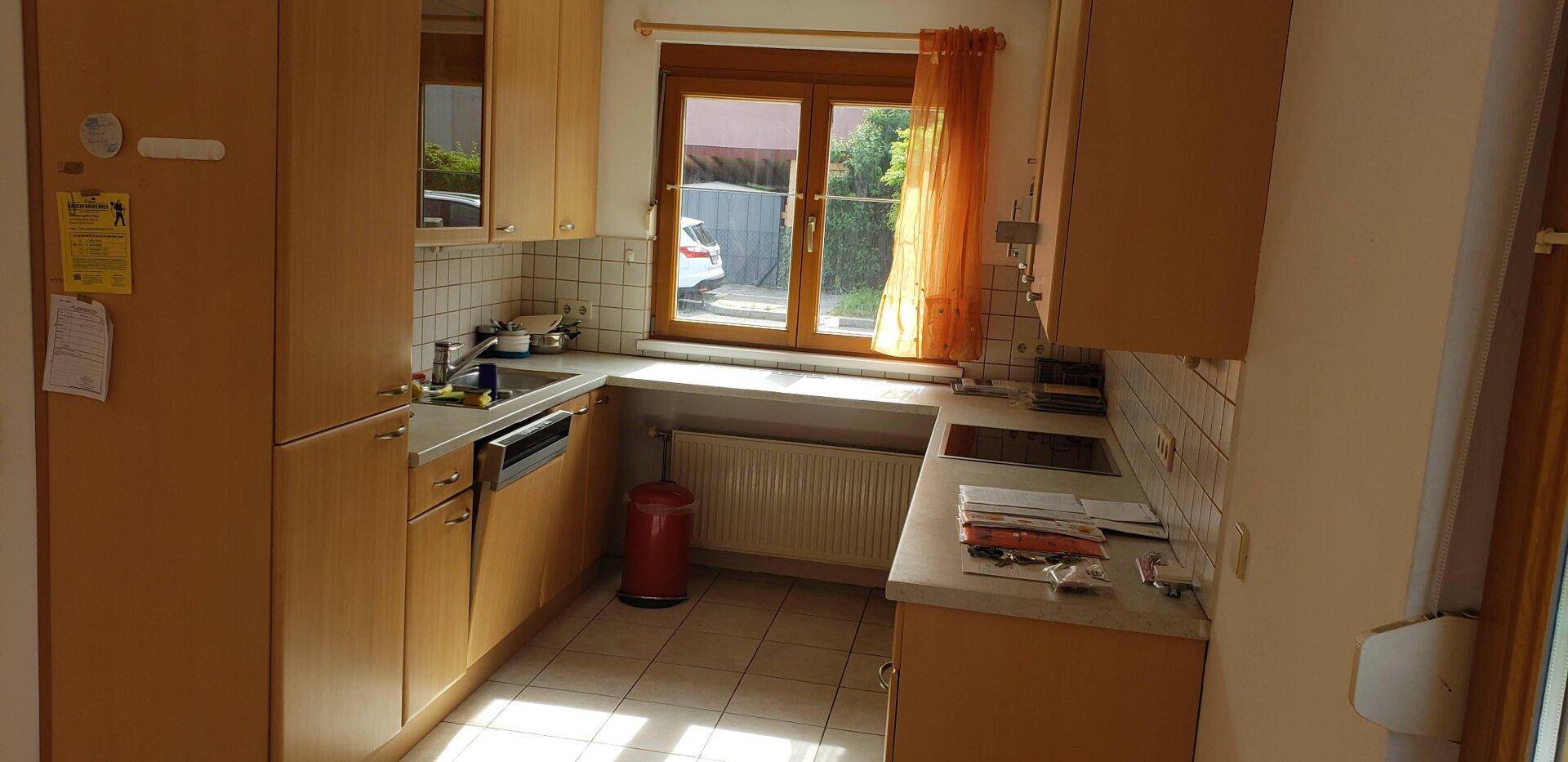 Voll ausgestattete Küche mit hellen Holzfronten, Fliesenboden und Fenster für Tageslicht.