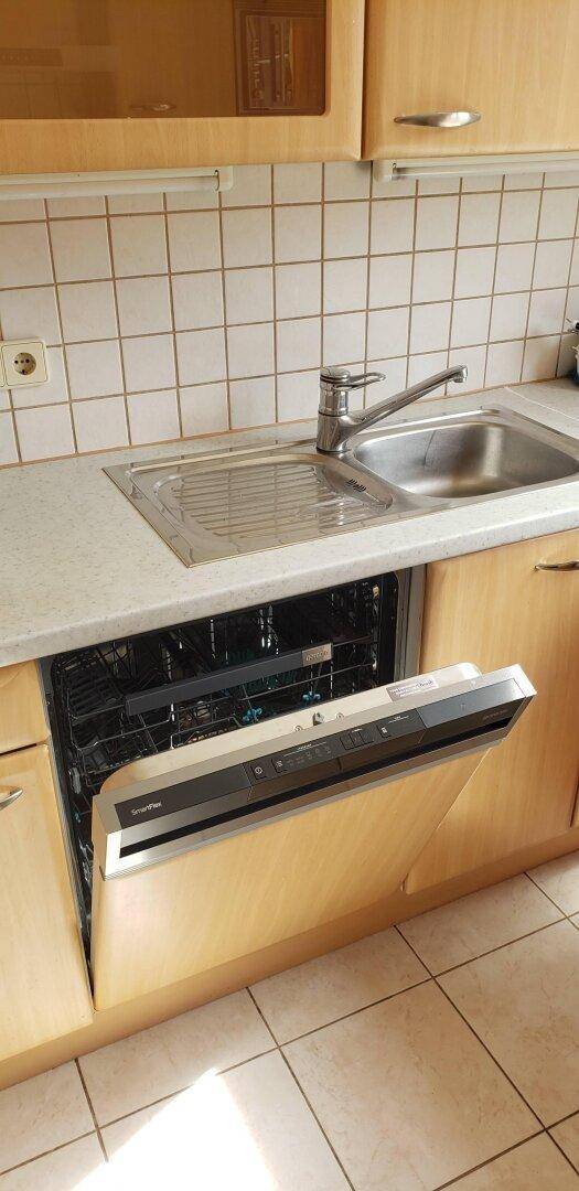 Integrierter Geschirrspüler in der Küche mit Spülbecken und hellen Holzschränken.
