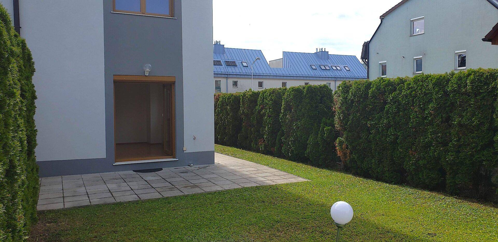 Gepflegter Gartenbereich mit kleiner Terrasse, Rasenfläche und hoher Hecke für Privatsphäre.
