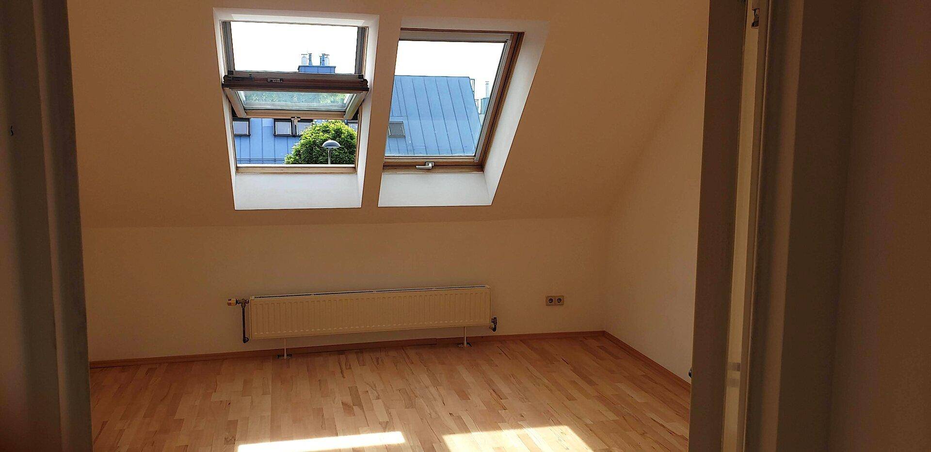 Geräumiges Dachzimmer mit Holzboden und viel Tageslicht durch die Dachfenster.