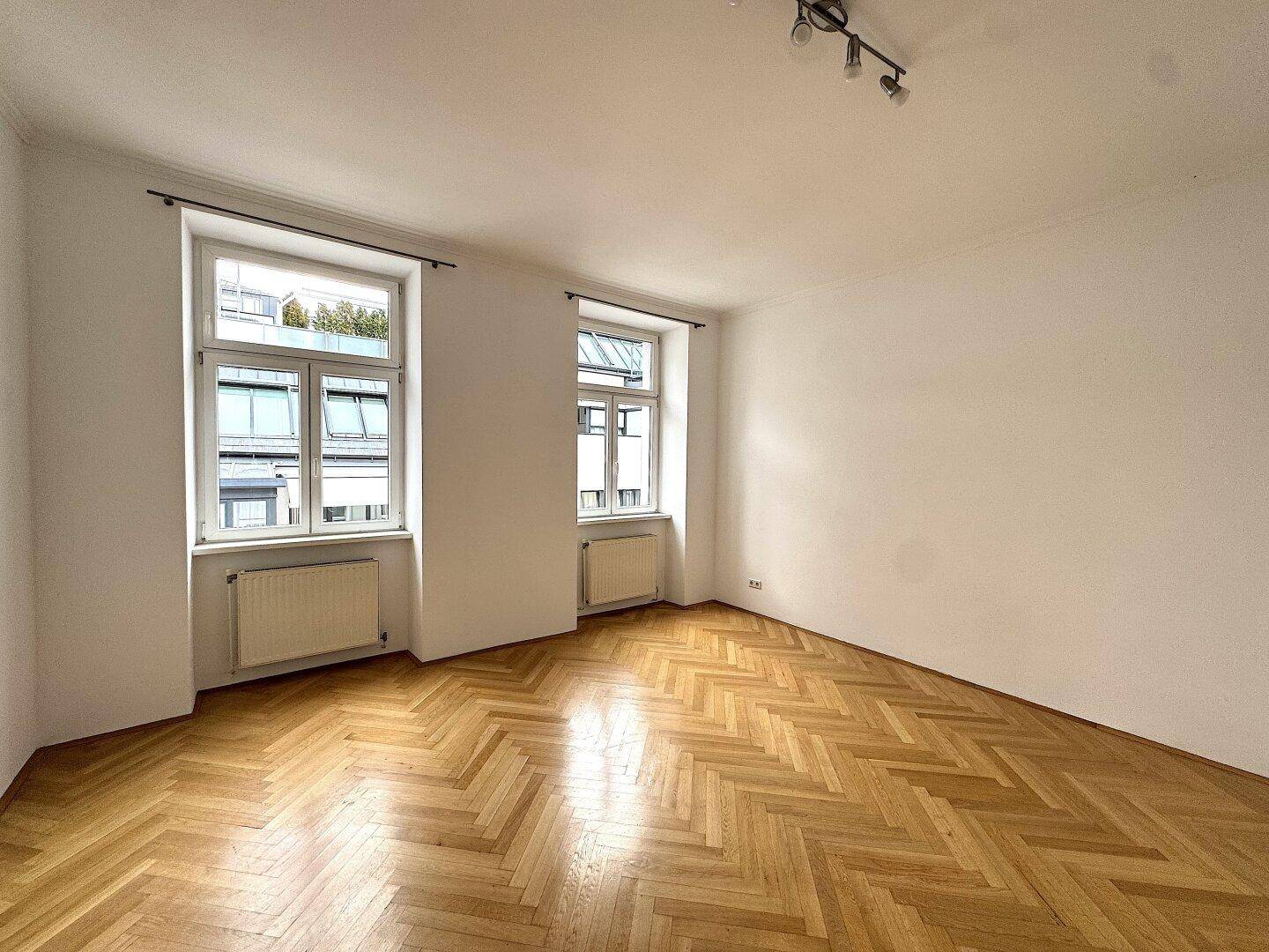 Lichtdurchflutetes Zimmer mit elegantem Fischgrätparkett und Blick auf die Umgebung.