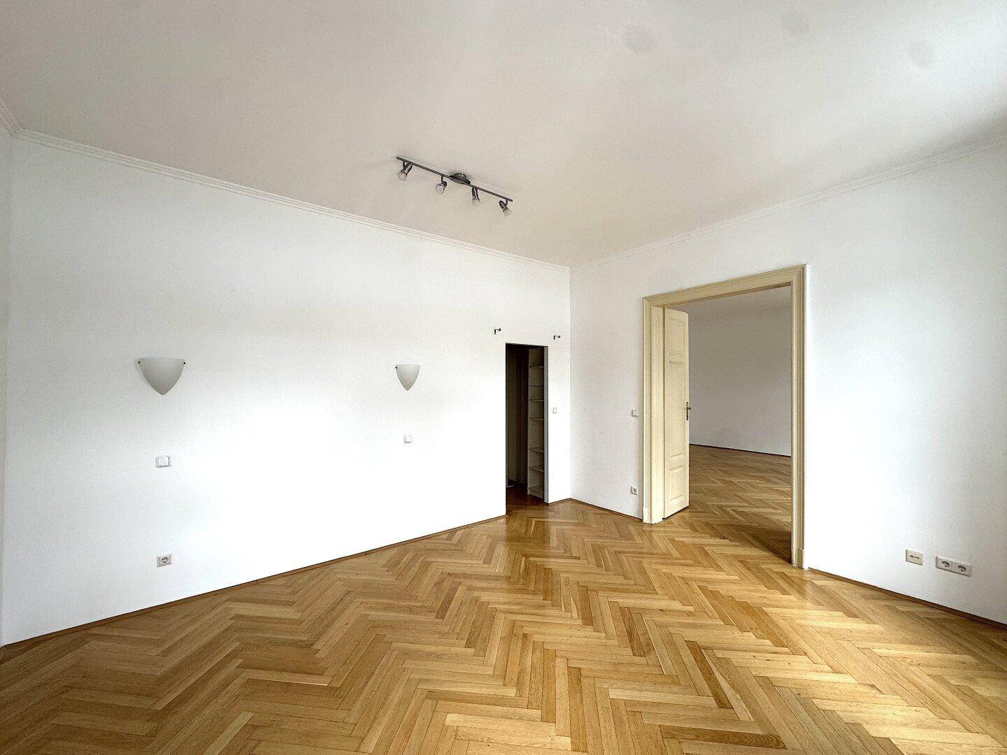 Geräumiges Zimmer mit Fischgrätparkett und offenem Zugang zu einem weiteren Raum.