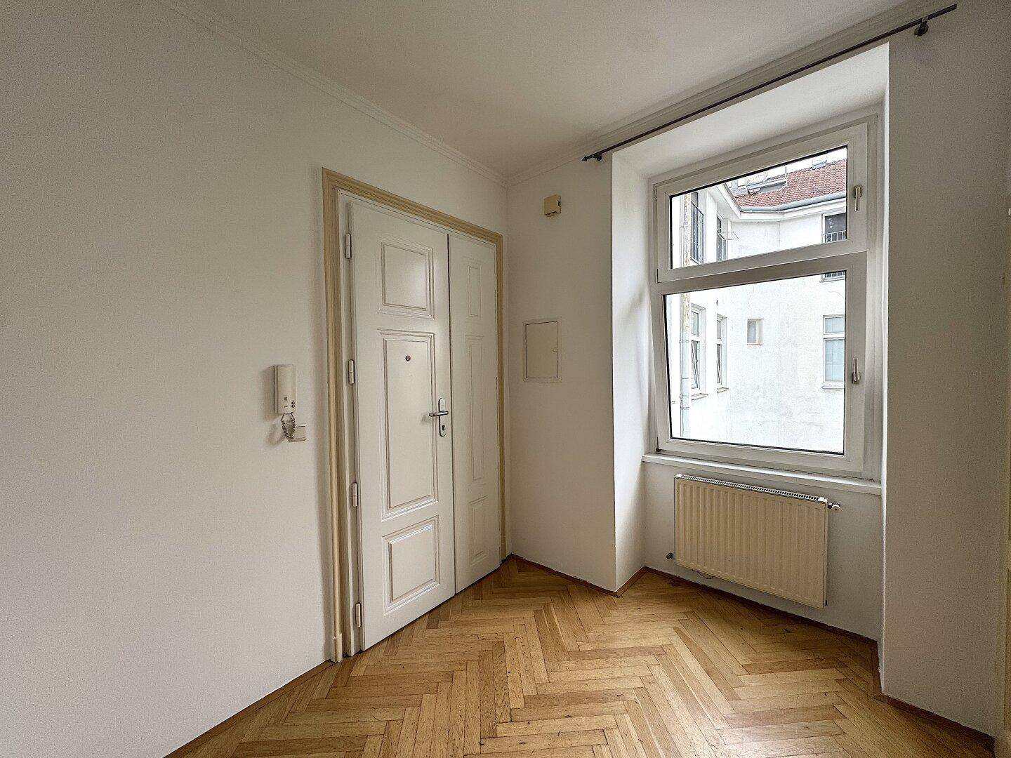Helles Zimmer mit Fischgrätparkett, großem Fenster und Flügeltür.
