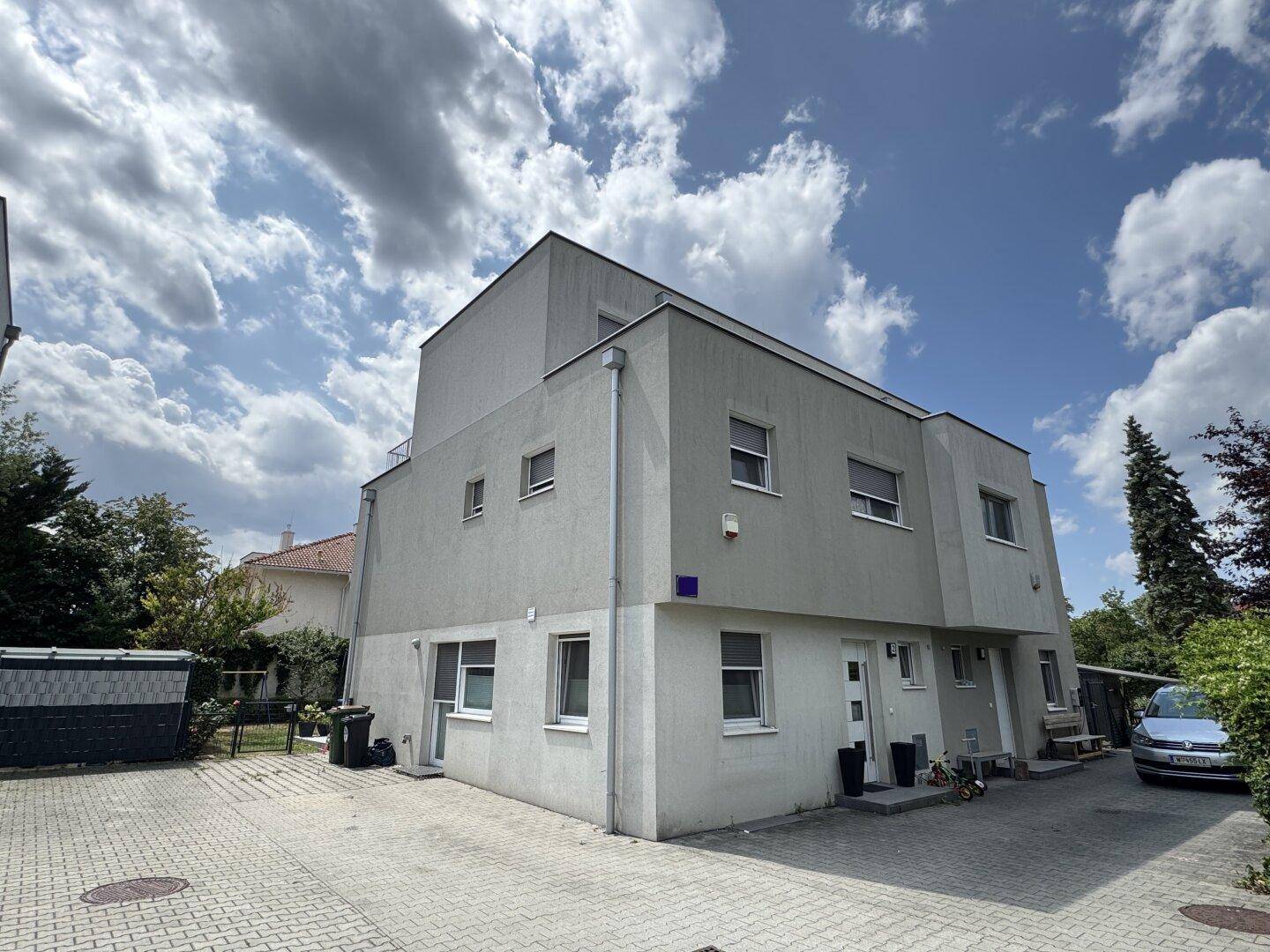 Modernes Gebäude mit grauer Fassade, vielen Fenstern und gepflasterter Auffahrt.