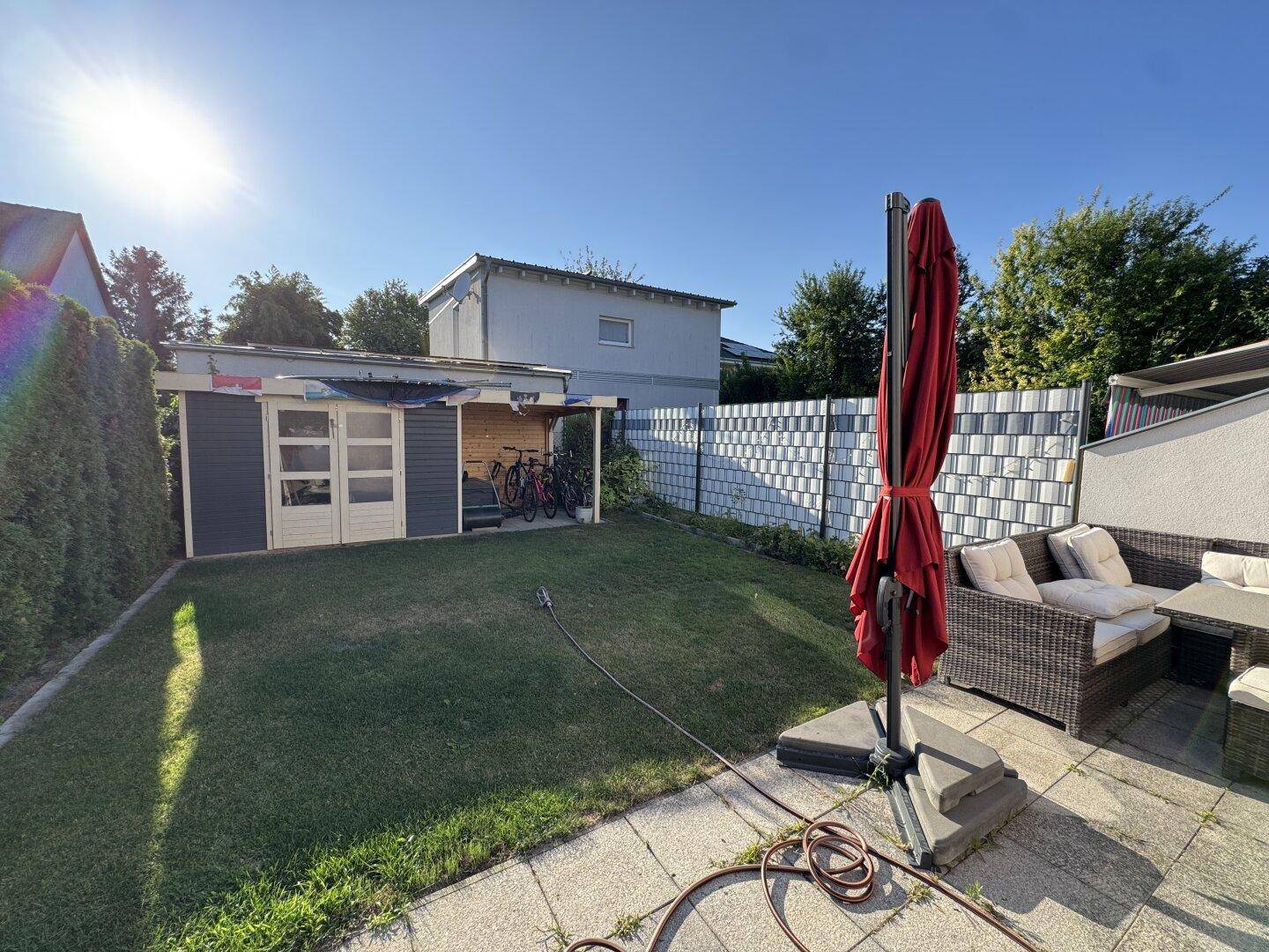 Sonniger Garten mit Rasenfläche, Terrasse und Gartenhaus, ideal für Entspannung im Freien.