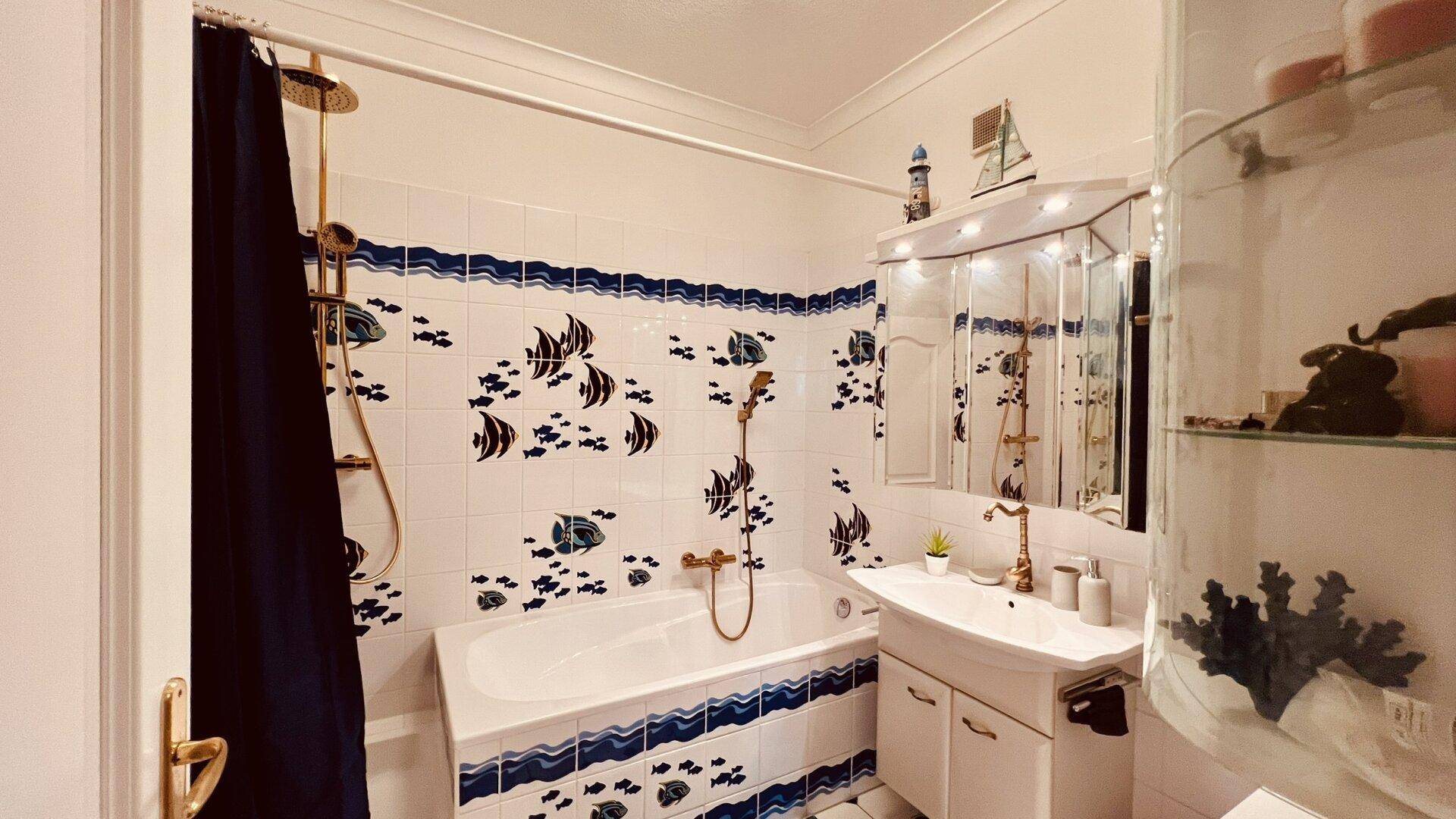 Badezimmer mit Badewanne, Dusche und verspielten blau-weißen Fliesen mit Fischmotiven.