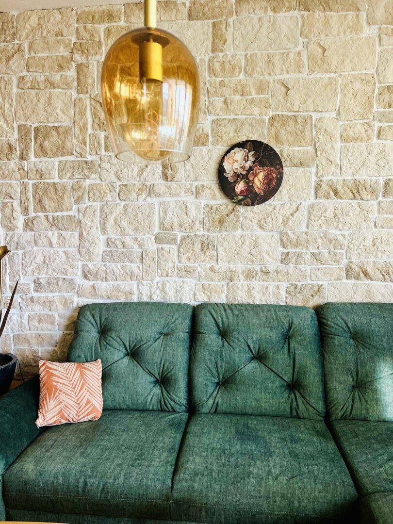 Detailansicht eines grünen Sofas vor einer rustikalen Steinwand mit Pendelleuchte.
