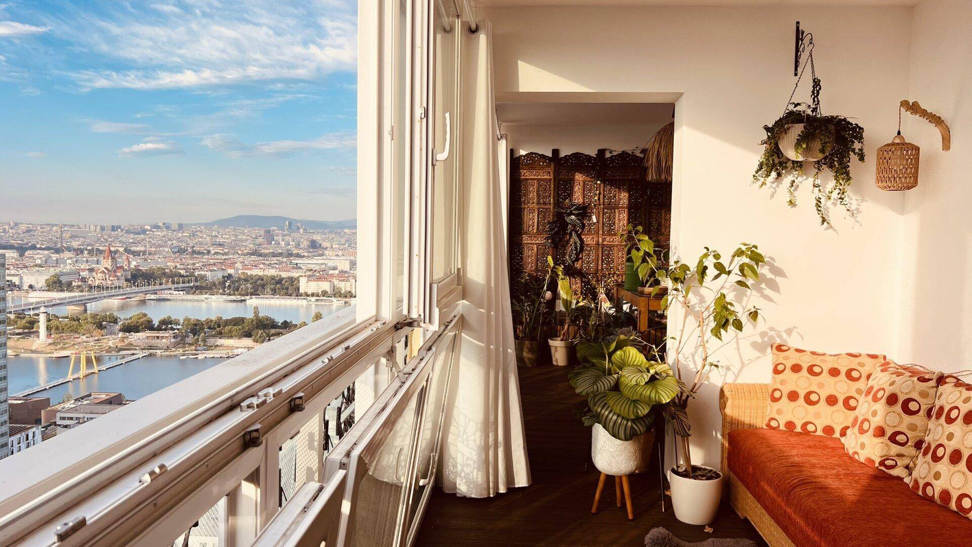 Heller verglaster Balkon mit Sitzgelegenheiten, Pflanzen und weitem Stadtblick.