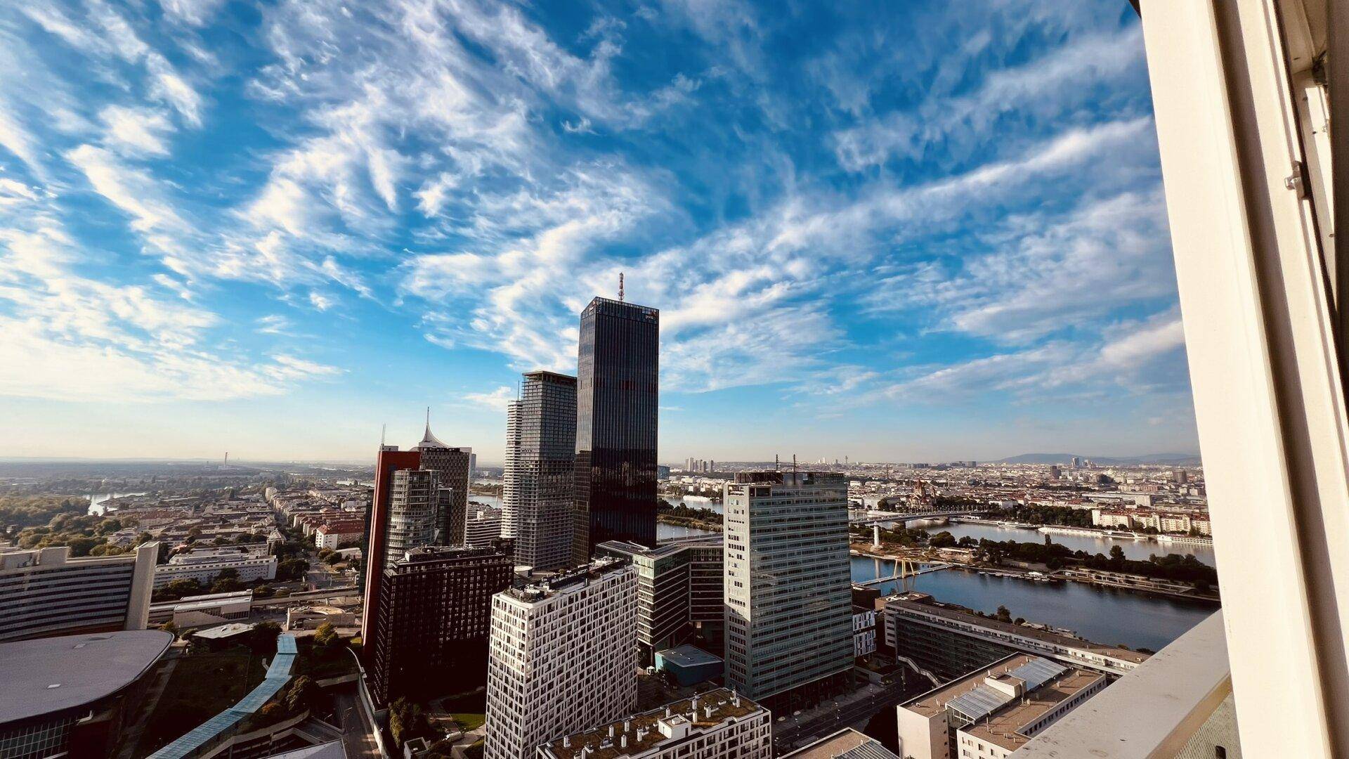 Panoramablick auf die Stadt mit modernen Hochhäusern, Fluss und weitem Horizont unter blauem Himmel.