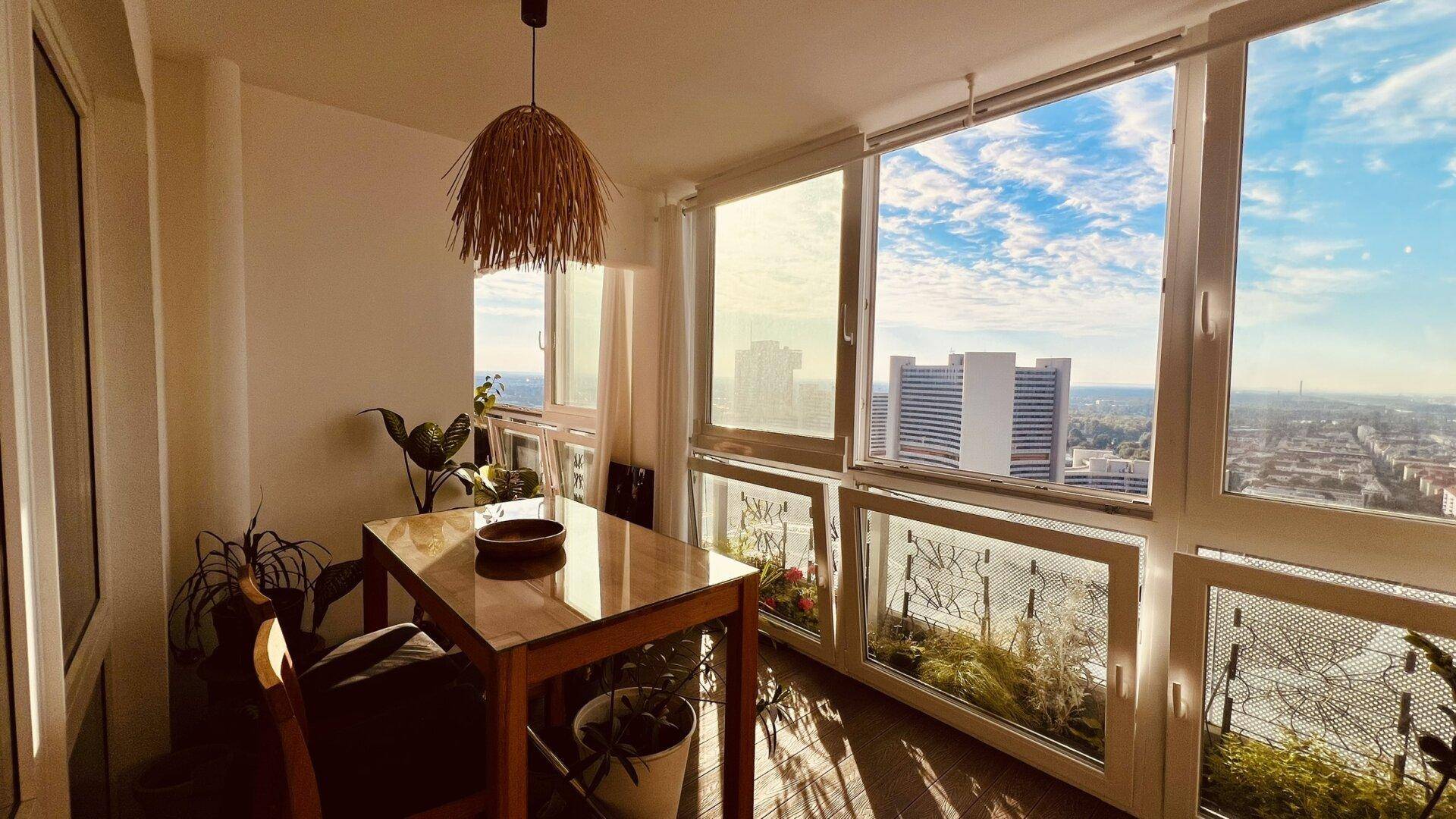 Heller verglaster Balkon mit Esstisch, Pflanzen und weitem Stadtblick.
