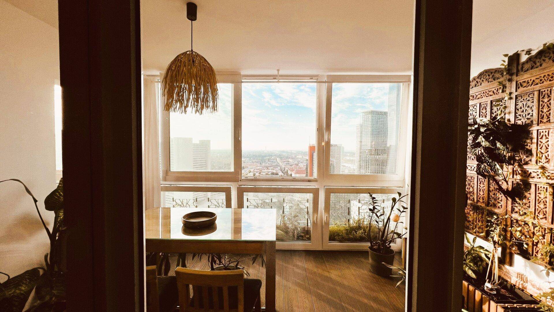 Heller verglaster Balkon mit Esstisch, Pflanzen und weitem Stadtblick.