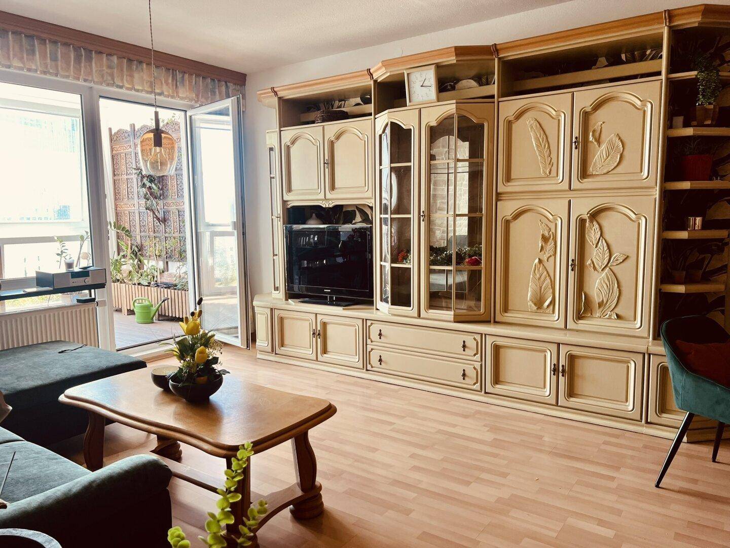 Wohnzimmer mit großer Schrankwand, Sofa und Zugang zu einem verglasten Balkon.
