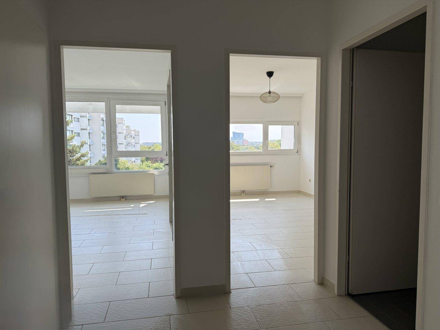 Heller Flur mit Blick in zwei angrenzende Zimmer, beide mit Fenstern und Heizkörpern.