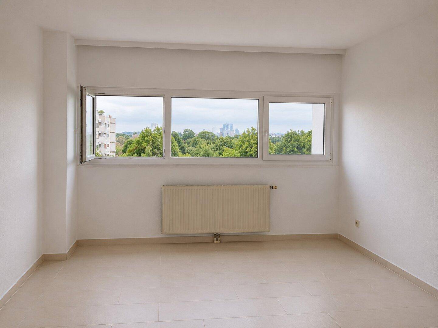 Helles Schlafzimmer mit Fliesenboden, Heizkörper und Blick ins Grüne mit Stadtkulisse.