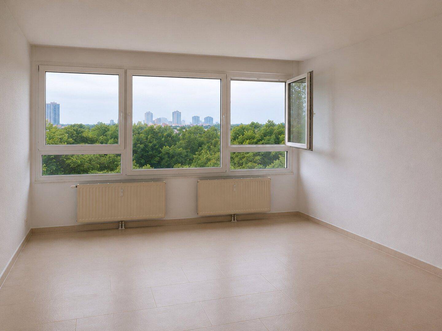 Geräumiges Zimmer mit Fliesenboden, zwei Heizkörpern und weitem Blick ins Grüne und auf die Stadt.