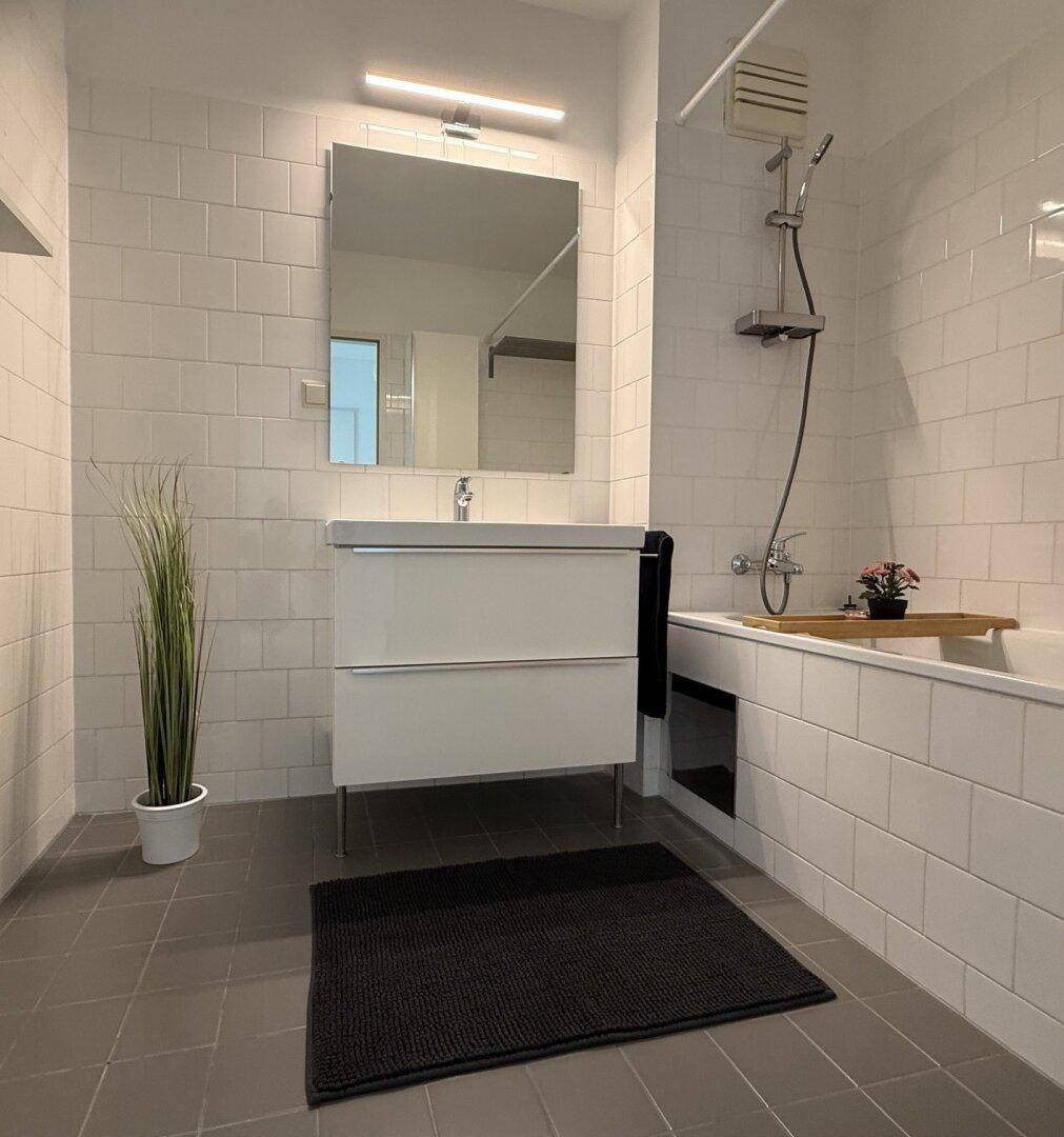 Modernes Badezimmer mit weißen Wandfliesen, dunklem Boden und Badewanne mit Duschfunktion.