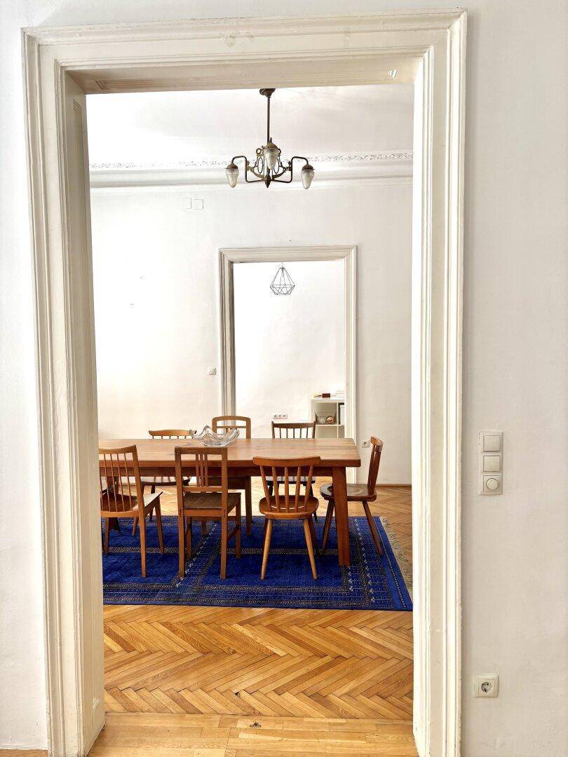 Blick durch eine Türöffnung in ein elegantes Esszimmer mit Holztisch und klassischem Parkettboden.