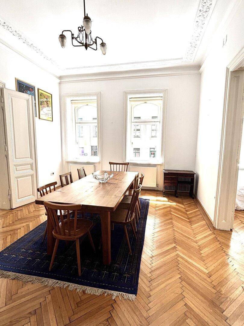 Geräumiges Esszimmer mit Fischgrätparkett, Stuckdecke und großem Holztisch für gesellige Runden.