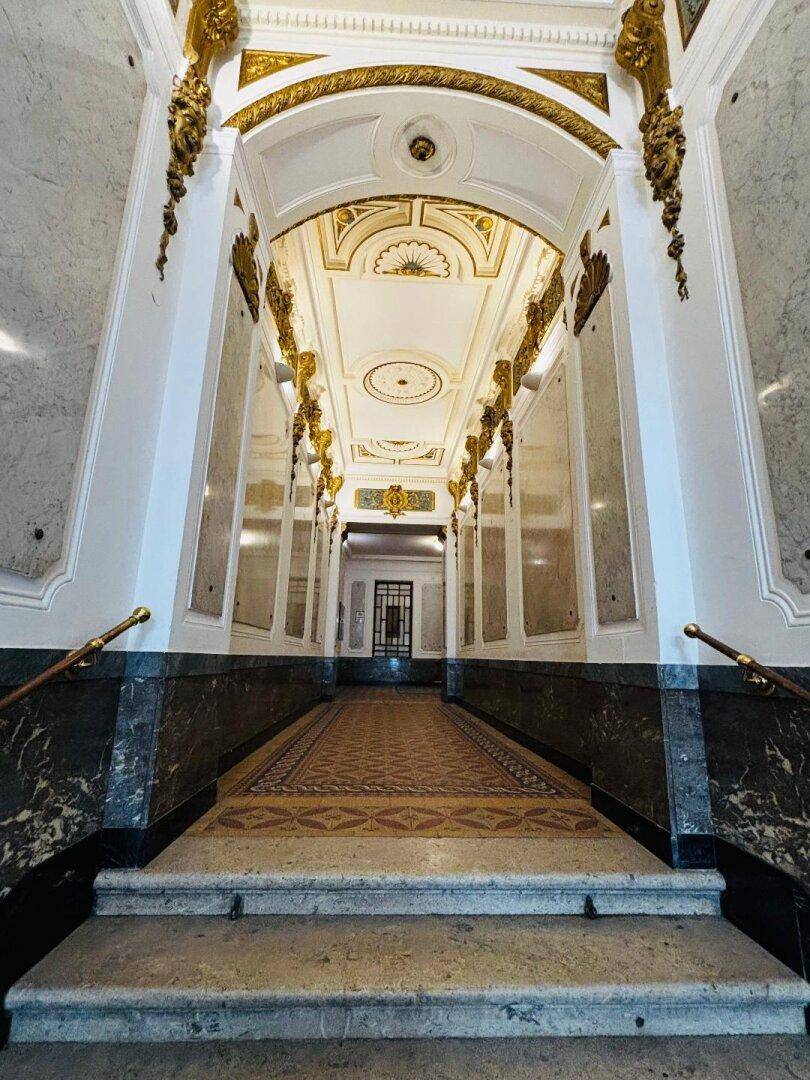 Prunkvoller Eingangsbereich mit hohen Decken, Marmorwänden und goldenen Verzierungen im klassischen Stil.