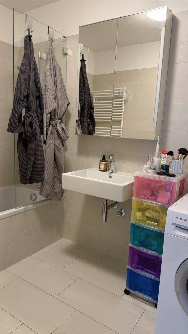 Modernes Badezimmer mit Waschbecken, Spiegelschrank, Badewanne und beheiztem Handtuchhalter.