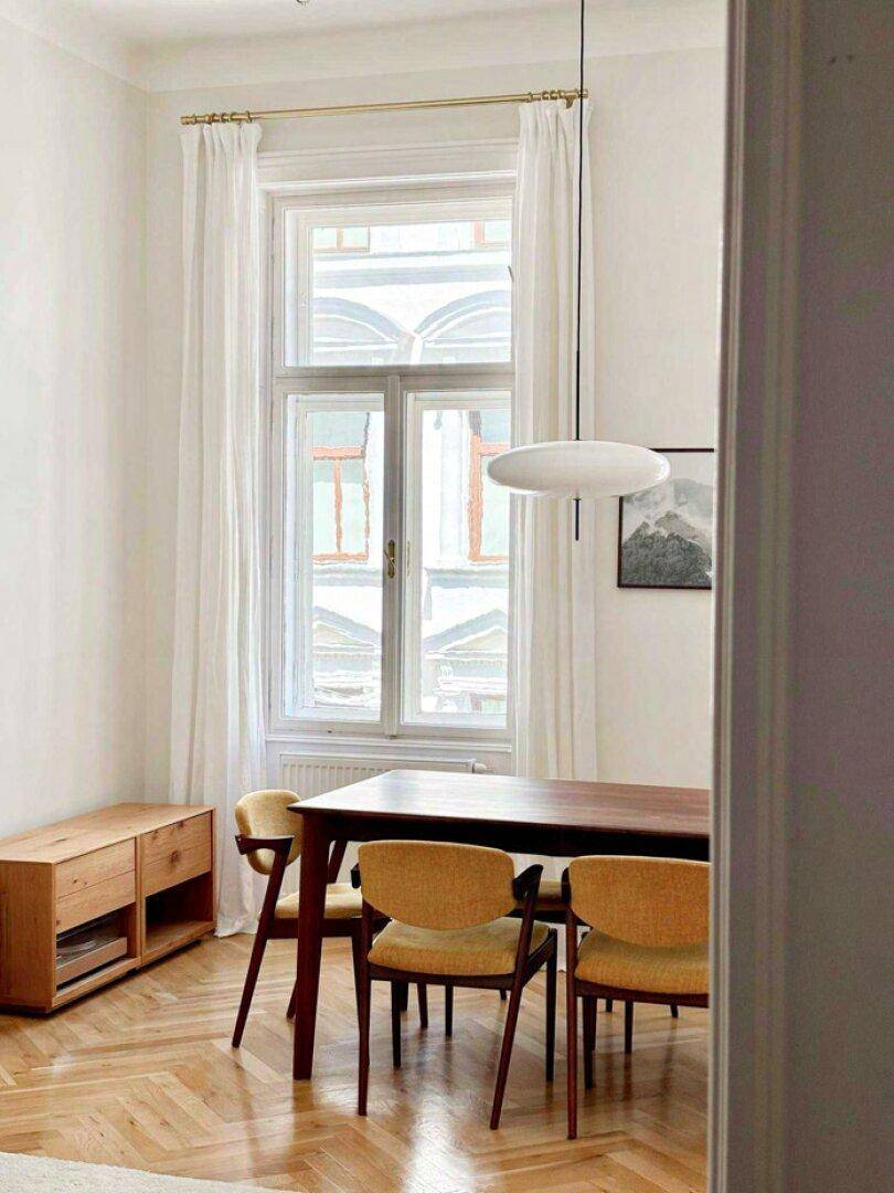 Heller Essbereich mit großem Fenster, Holztisch und modernen Stühlen auf Fischgrätparkett.