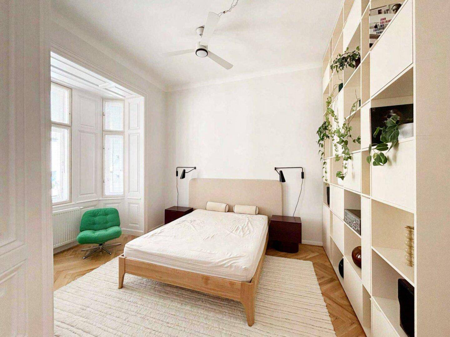 Helles Schlafzimmer mit Holzbett, integriertem Bücherregal und Fischgrätparkettboden.