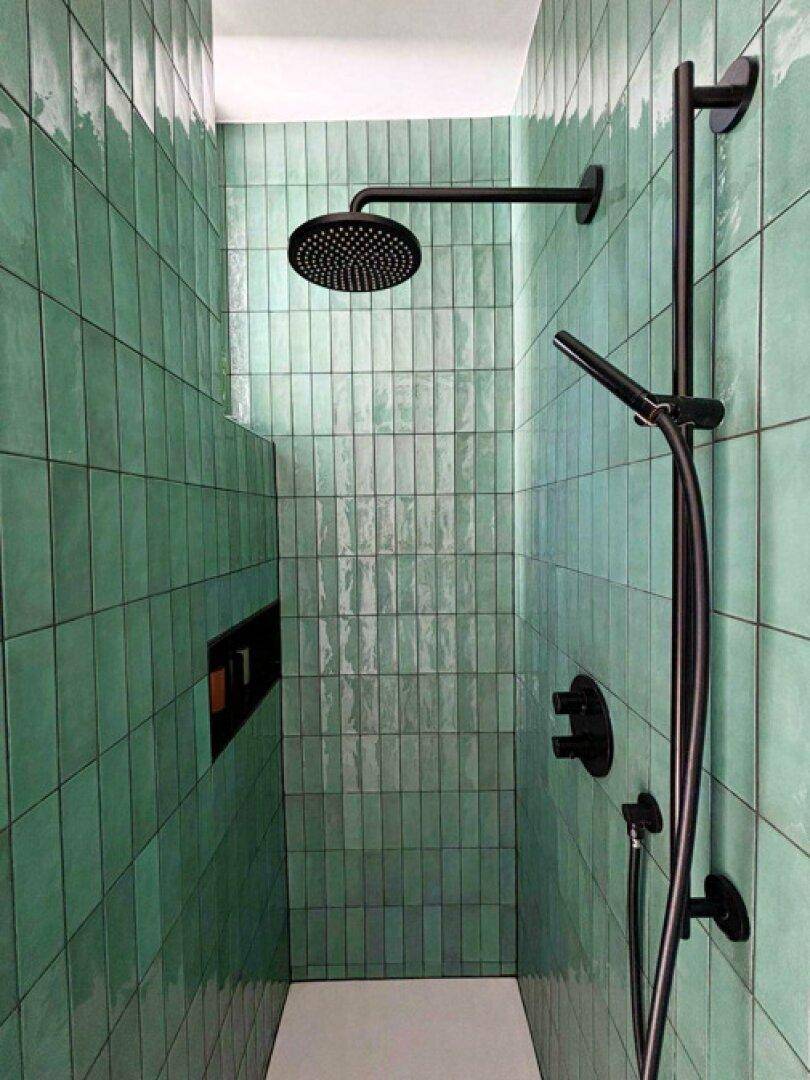 Moderne begehbare Dusche mit grünen Fliesen und schwarzer Armatur, die ein stilvolles Ambiente schafft.