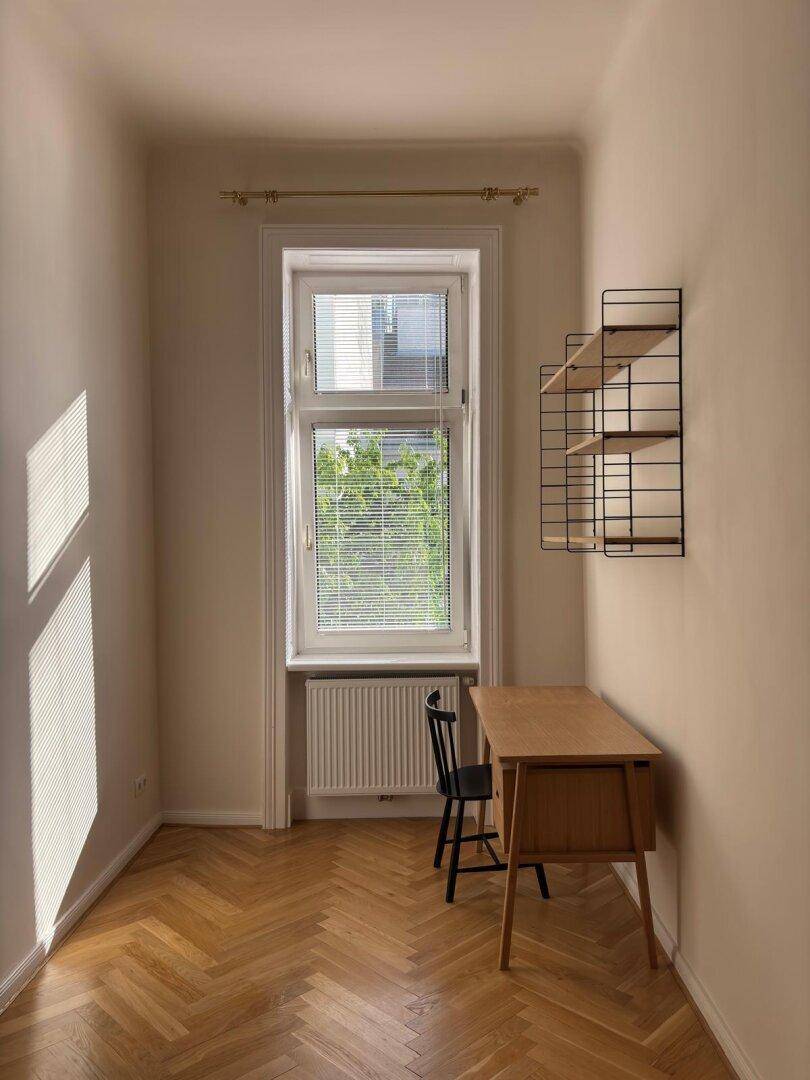Helles Arbeitszimmer mit Fischgrätparkett, Schreibtisch und Blick ins Grüne durch das Fenster.