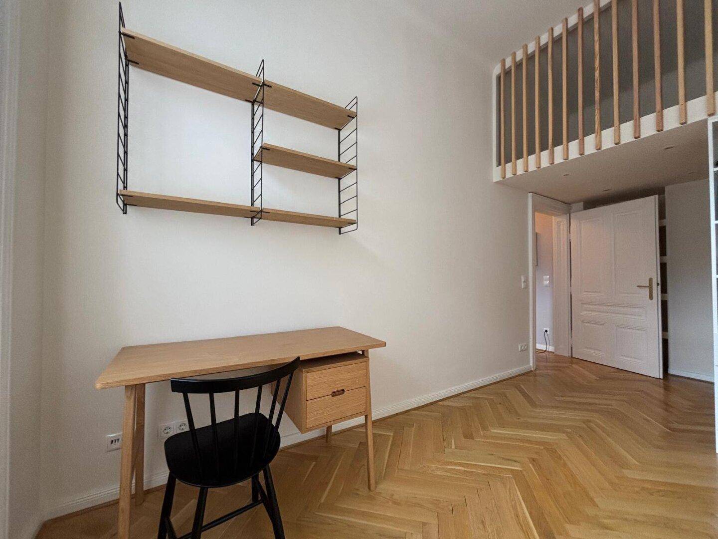 Arbeitszimmer mit hohen Decken, Fischgrätparkett und integriertem Regal unter einer Galerie.