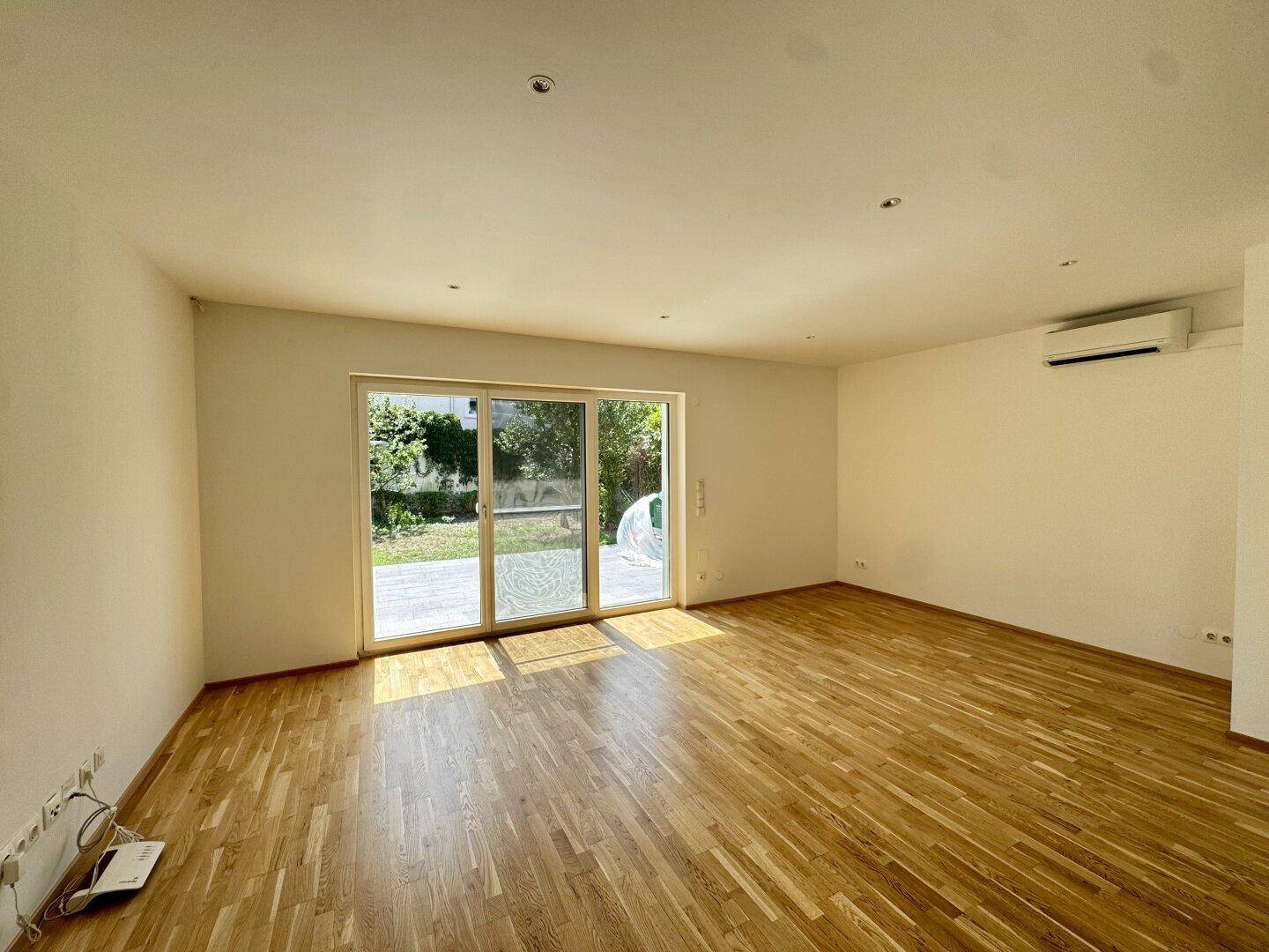 Geräumiges Wohnzimmer mit Holzboden, großen Schiebetüren und Klimaanlage.