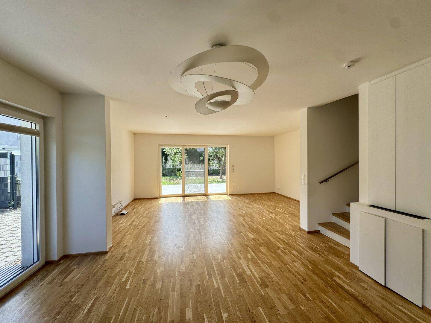 Geräumiges Wohnzimmer mit Parkettboden, moderner Deckenleuchte und direktem Gartenzugang.
