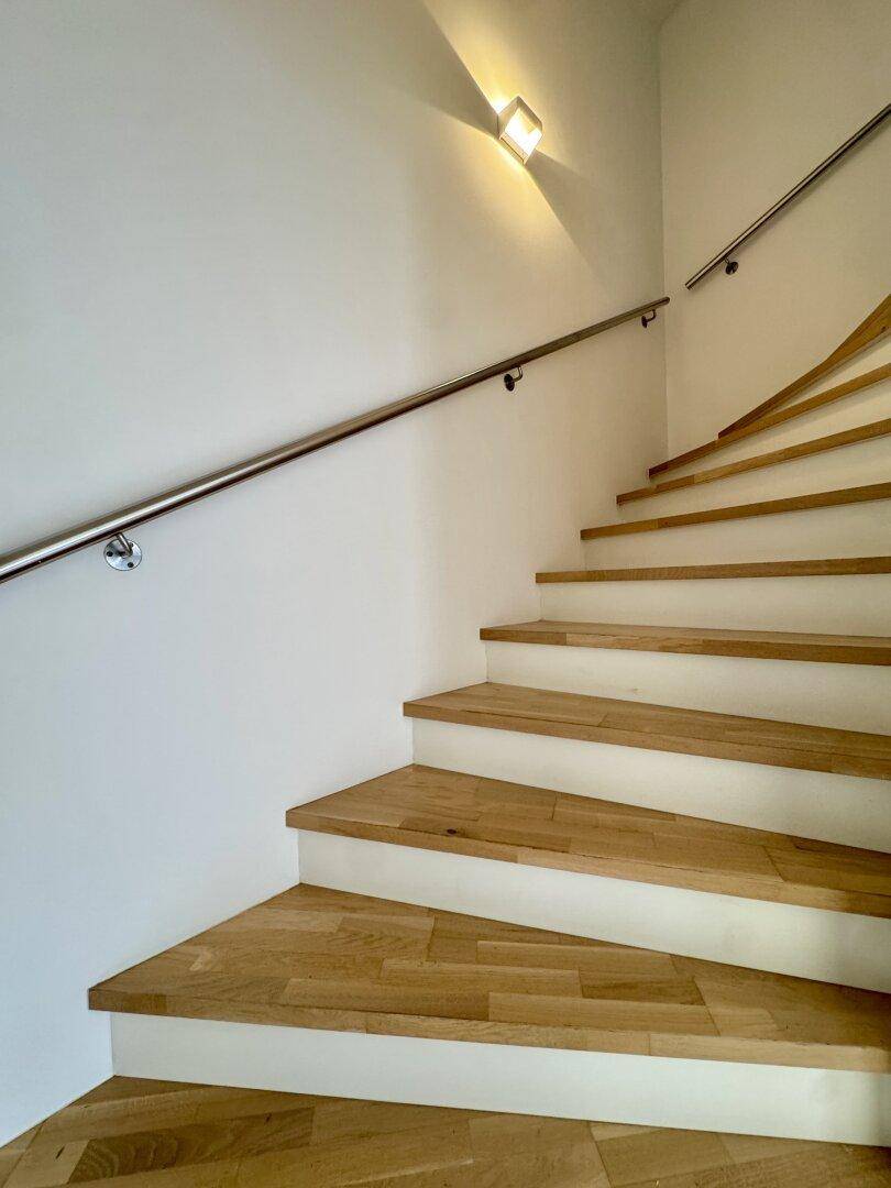Moderne Holztreppe mit elegantem Metallgeländer, führt in die obere Etage.