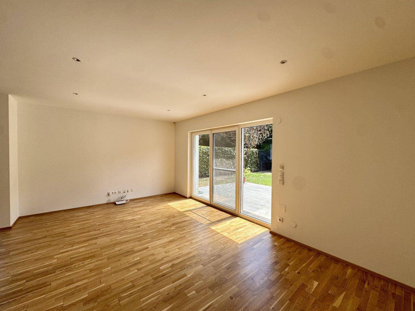 Heller Raum mit Parkettboden und großen Schiebetüren zum Garten, durchflutet von Sonnenlicht.