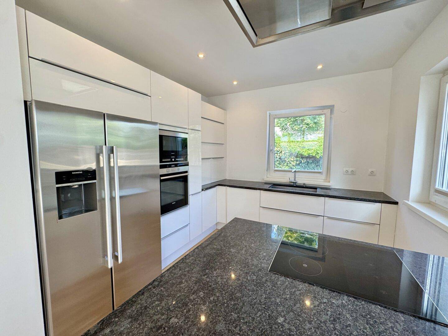 Helle Küche mit großem Kühlschrank, Kochinsel und modernen weißen Schränken.