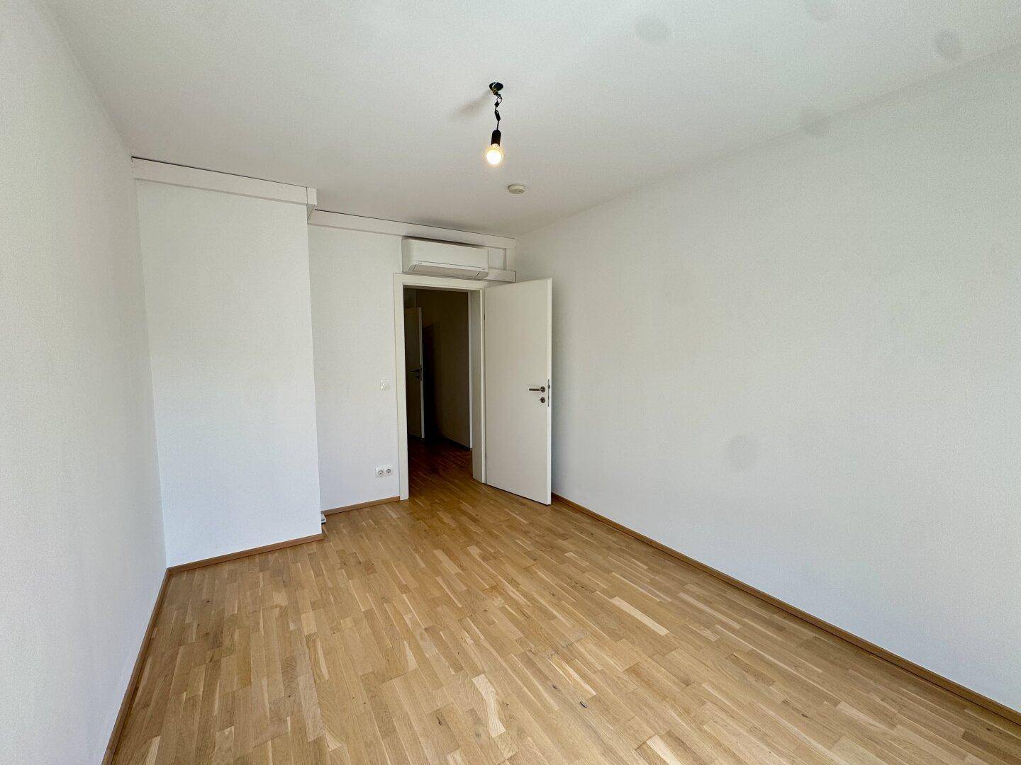 Geräumiges Schlafzimmer mit Parkettboden, Klimaanlage und weißer Tür.
